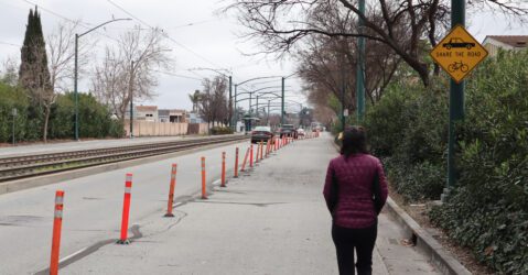Woman in puffer jacket walks in blocked pedestrian lane while cars drive on the open lanes, with a "share the road" sign above her