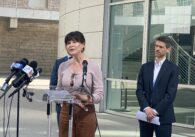 A woman speaks into microphones at a podium