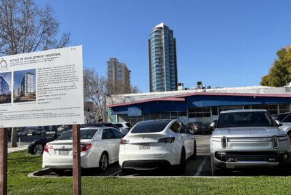A parking lot with a development project sign in the foreground