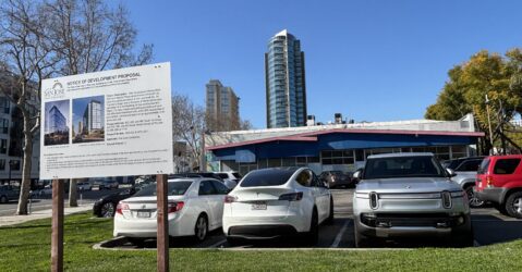A parking lot with a development project sign in the foreground