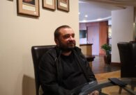 Man black jacket sitting at glass table in lobby setting