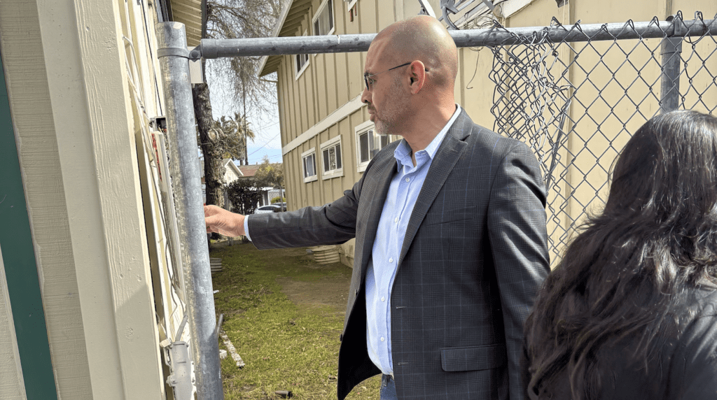 A man with glasses inspecting a piece of cut up fencing.