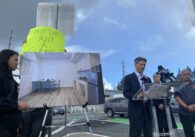 A man in a suit stands outside speaking at a podium