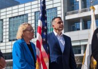An older woman and middle-aged man stand next to an American flag