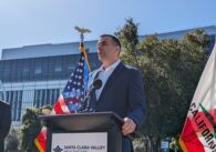 A man in a suit stands outside speaking at a podium