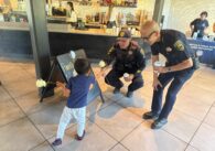 Phan Ngo, a bald tan Asian man wearing glasses and a Public Safety Officer uniform, squatting beside a tan child holding two yellow roses.