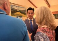 A man in a suit speaks to two people with their backs to the camera