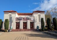 The outside of a white theater with a terracotta Spanish-style roof.