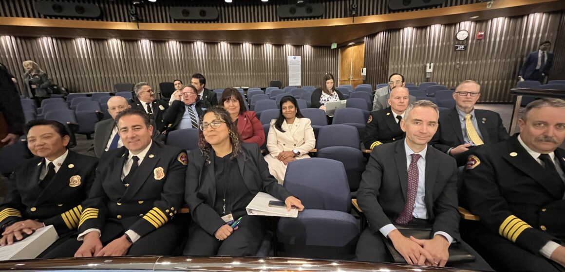 A group of firefighters sitting in the chambers of a government meeting