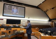 A man in a suit speaks at a podium during a government meeting