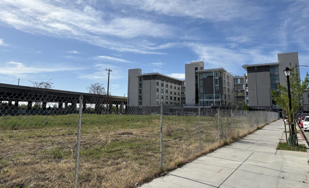 A large empty field beside three large towers and a freeway.