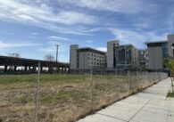 A large empty field beside three large towers and a freeway.