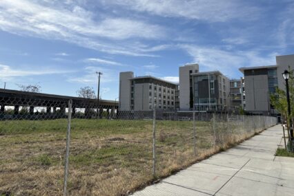 A large empty field beside three large towers and a freeway.