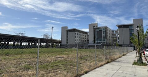 A large empty field beside three large towers and a freeway.