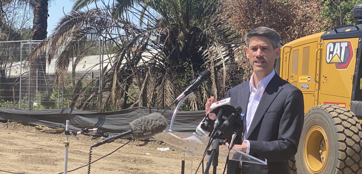 A man in a suit speaks at a podium at a construction site in San Jose