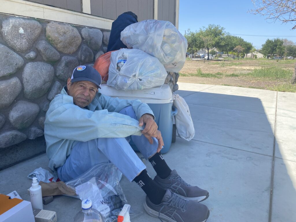 A homeless man sitting on the sidewalk with bags of his belongings