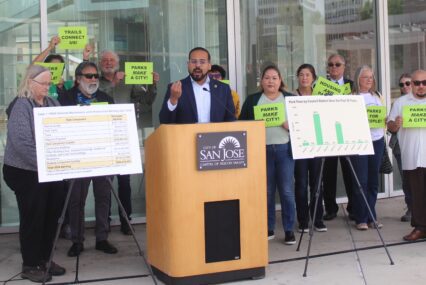 San Jose parks advocates rallied outside City Hall on April 15, 2025 ahead of a City Council discussion over a potential ballot measure benefiting parks funding, with one man standing in front of a podium surrounded by supporters.