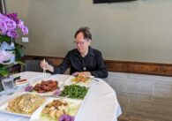 An older man sits at a table with four plates of food