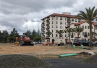 An empty field with bulldozers and a six-story building in the background