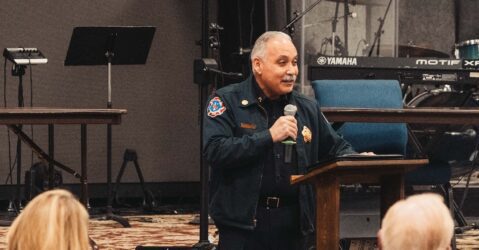 San Jose's fire chief speaks to a crowd indoors holding a microphone