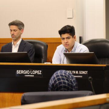 Matt Mahan, a white man with light skin wearing a blue blazer and white button down shirt, sitting beside Sergio Lopez, a tanned Latino man wearing a blue button down, sitting beside Carolyn Gonot, a white woman with reddish hair in a bob wearing a pink blazer, all sitting behind a raised dias
