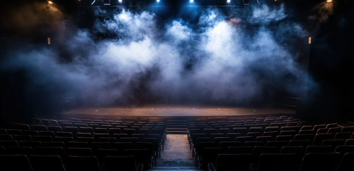 A dramatic theatre stage filled with illuminated smoke and rows of seating