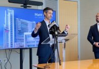 A man in a suit stands at a podium speaking into a microphone