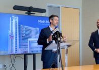 A man stands at a podium in front of a television