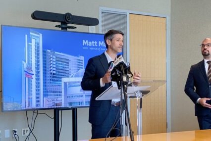 A man stands at a podium in front of a television