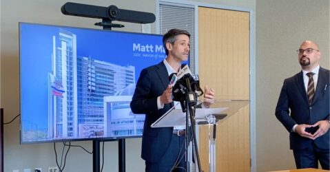 Un hombre se encuentra en un podio frente a un televisor.