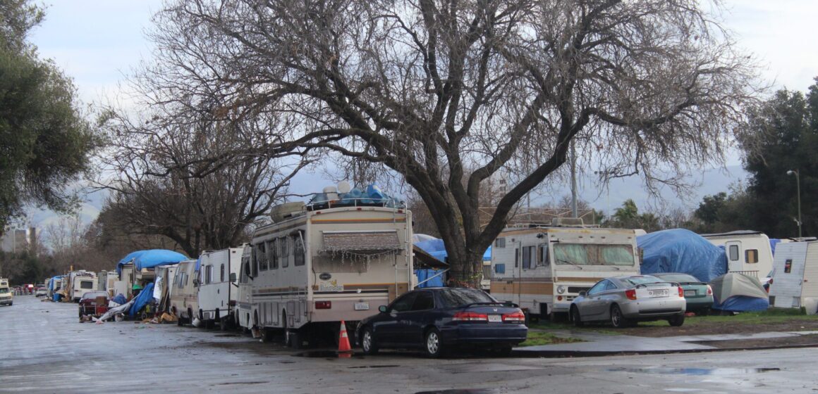 An encampment of RVs on the corner of a desolate street.