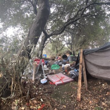 Homeless encampment San Jose Coyote Creek A makeshift tarp tent under a tree near a creek in San Jose, California