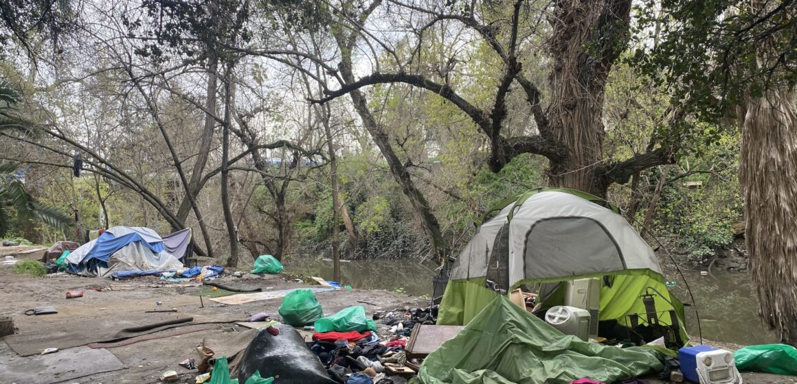 A homeless person's tent and belongings next to a creek
