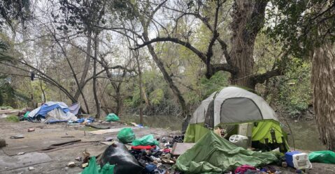 A homeless person's tent and belongings next to a creek