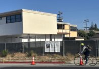 A vacant building in the background with a shady road in the foreground.