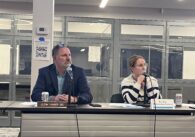 A man and woman sit at a desk at a local school board meeting