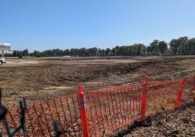A vast, empty dirt lot with orange construction bollards at the entrance.