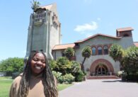 A woman stands in front of a clock tower on the campus of San Jose State University
