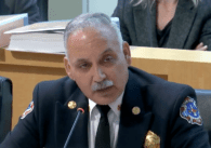 A man in a firefighter uniform speaking in front of a microphone.