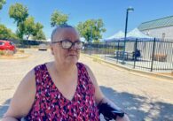 A woman wearing glasses sits outside in the shade