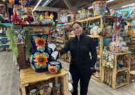 A woman stands in her shop next to pottery made in Mexico