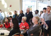 A group of people, some standing and some sitting, crowd around a circular table in a community room