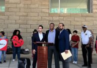 Three men standing at a podium, with a line of people standing behind them
