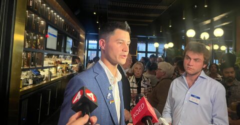 A man in a suit speaking into microphones inside a bar