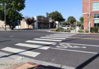 Paso de peatones con franjas blancas frente a un centro comercial peatonal