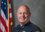 A public safety officer posing for a photo in front of an American flag