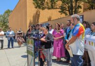 A woman wearing a bun and striped pants speaks into a microphone in front of a crowd of people.