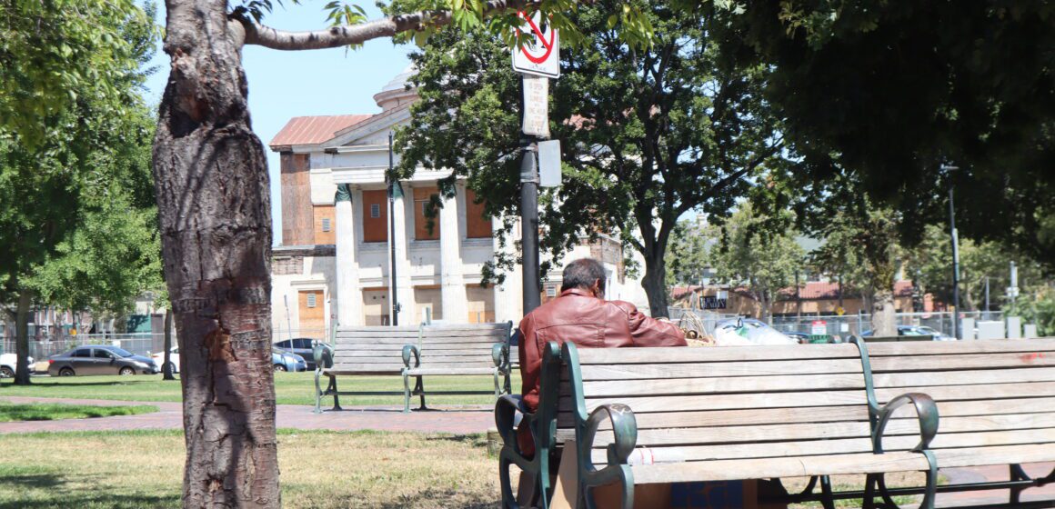 A homeless person sits on a park bench in San Jose, California