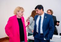 A woman in a pink blazer speaks to a man in a blue suit