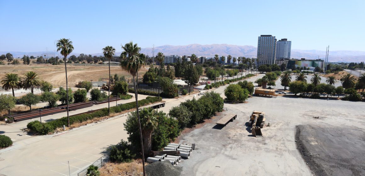 Photo of a large swathe of empty land with some construction equipment and apartment buildings in the background
